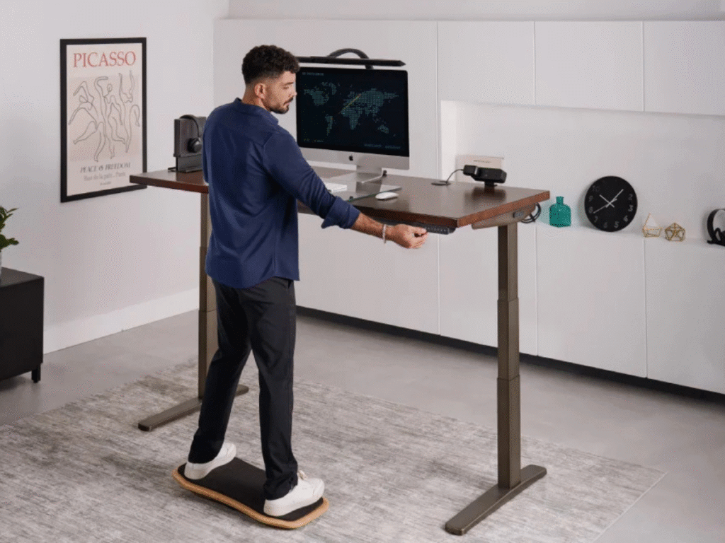 person standing working on an adjustable sit stand desk while standing